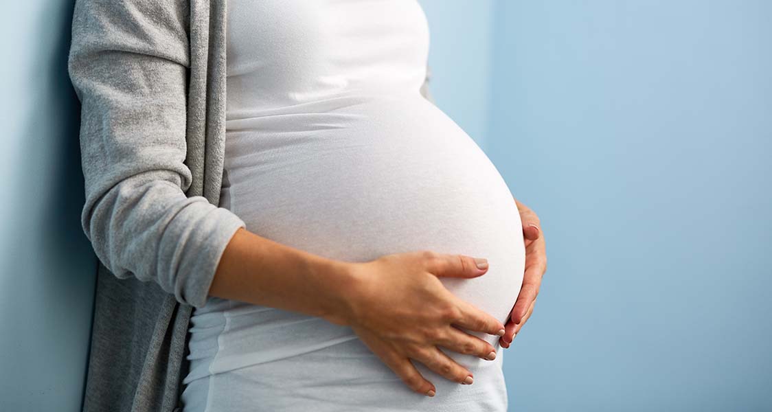 Pregnant woman leaning up against a wall holding her stomach.