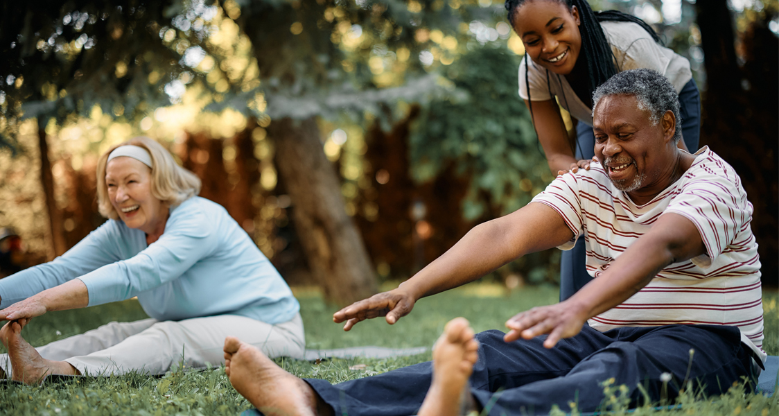 Happy black physical therapist assists seniors during exercise class in park.