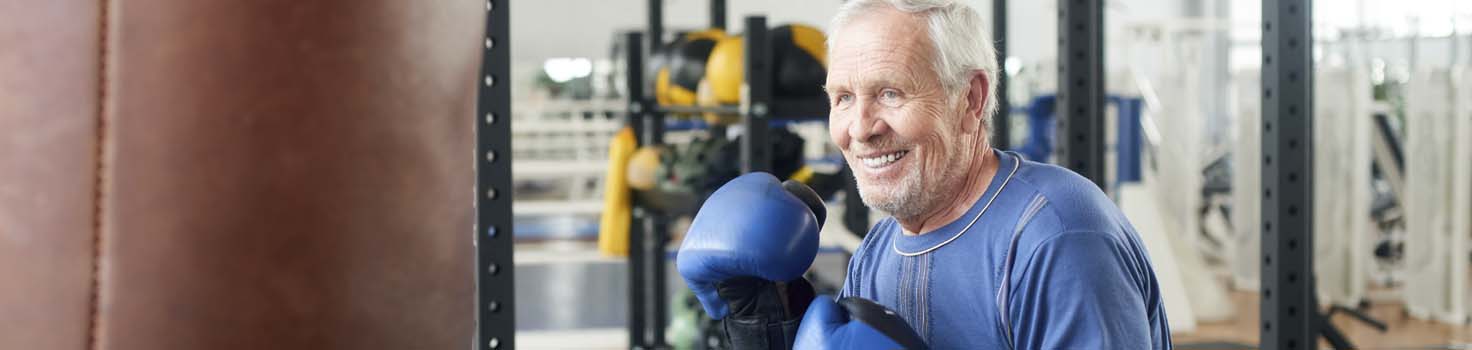 Handsome senior male training with punching bag. Old trainer training with punching bag in fitness studio. People, sport, active way of life.