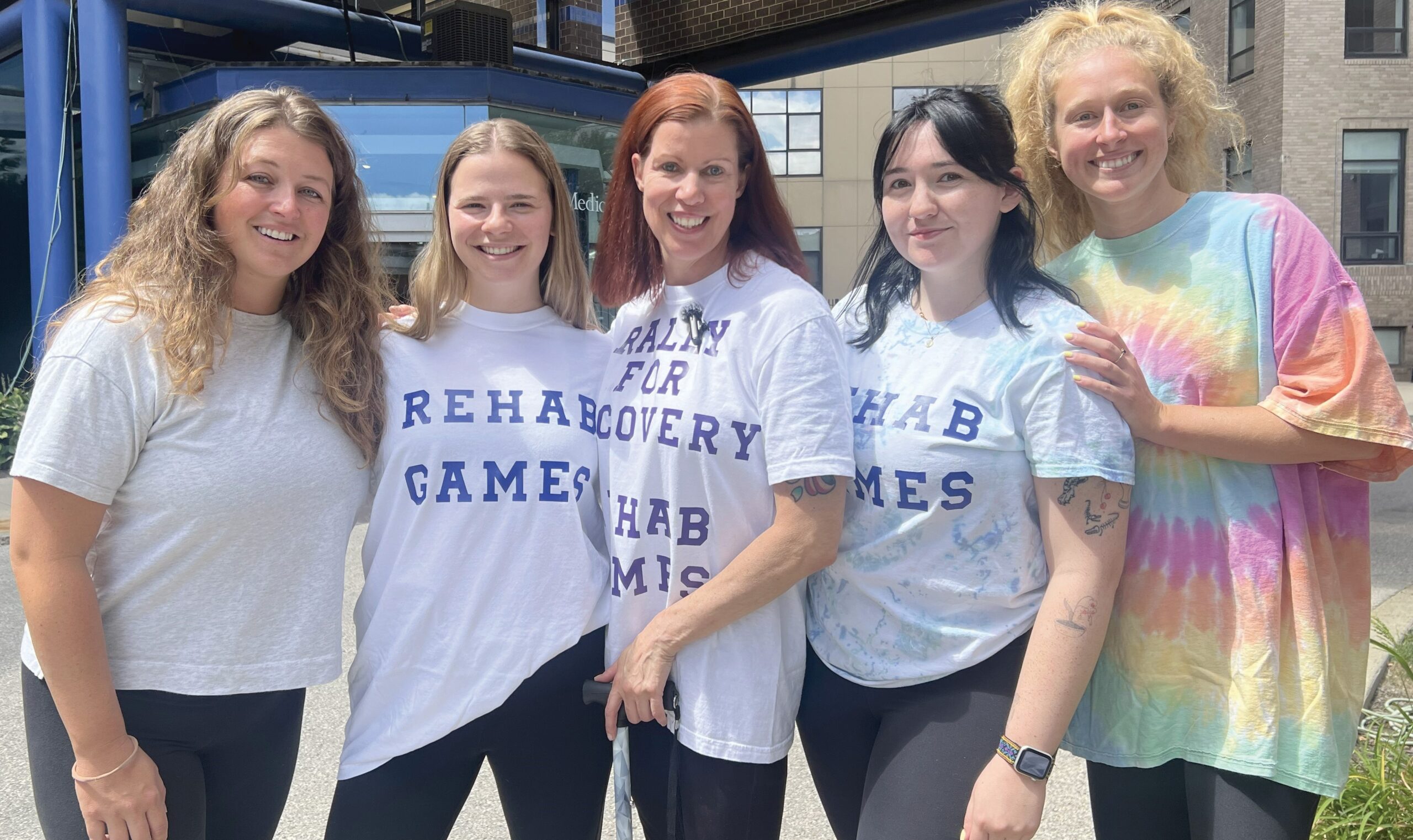 Five individuals standing outside of GSPP Rehabilitation's building wearing Rehab Games shirts and smiling