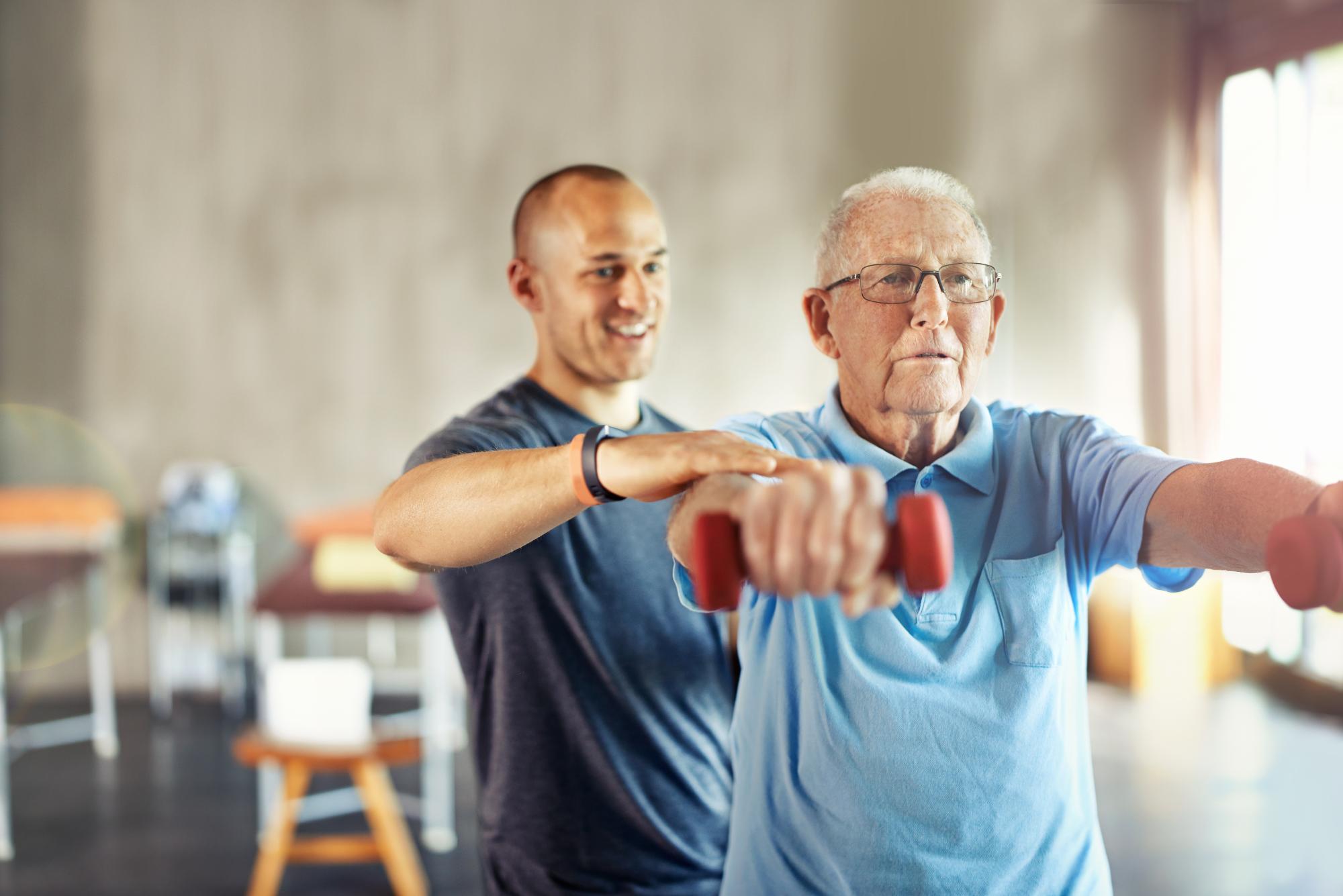 A senior lifts colorful hand weights while a trained professional guides