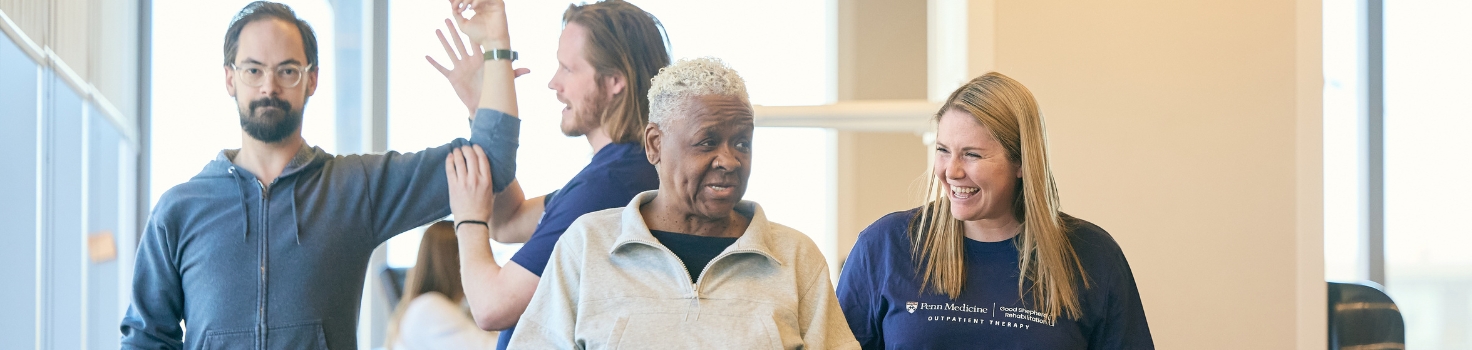 Photo showing Penn Medicine | Good Shepherd Rehabilitation Outpatient Therapy, a service of GSPP Rehabilitation, in action. Physical therapists work with patients who are doing exercises. Two people in the foreground are talking and smiling and laughing