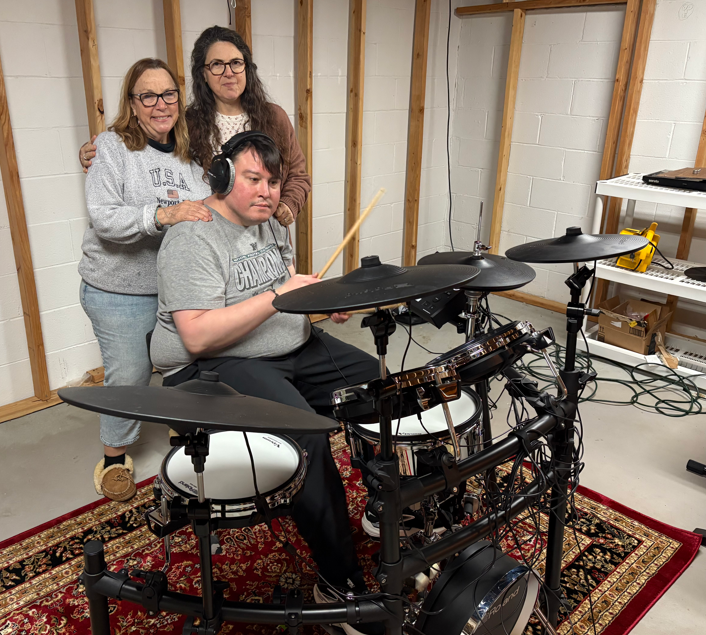 Christine (left) and sons step mom (right) smiling while her son is drumming.