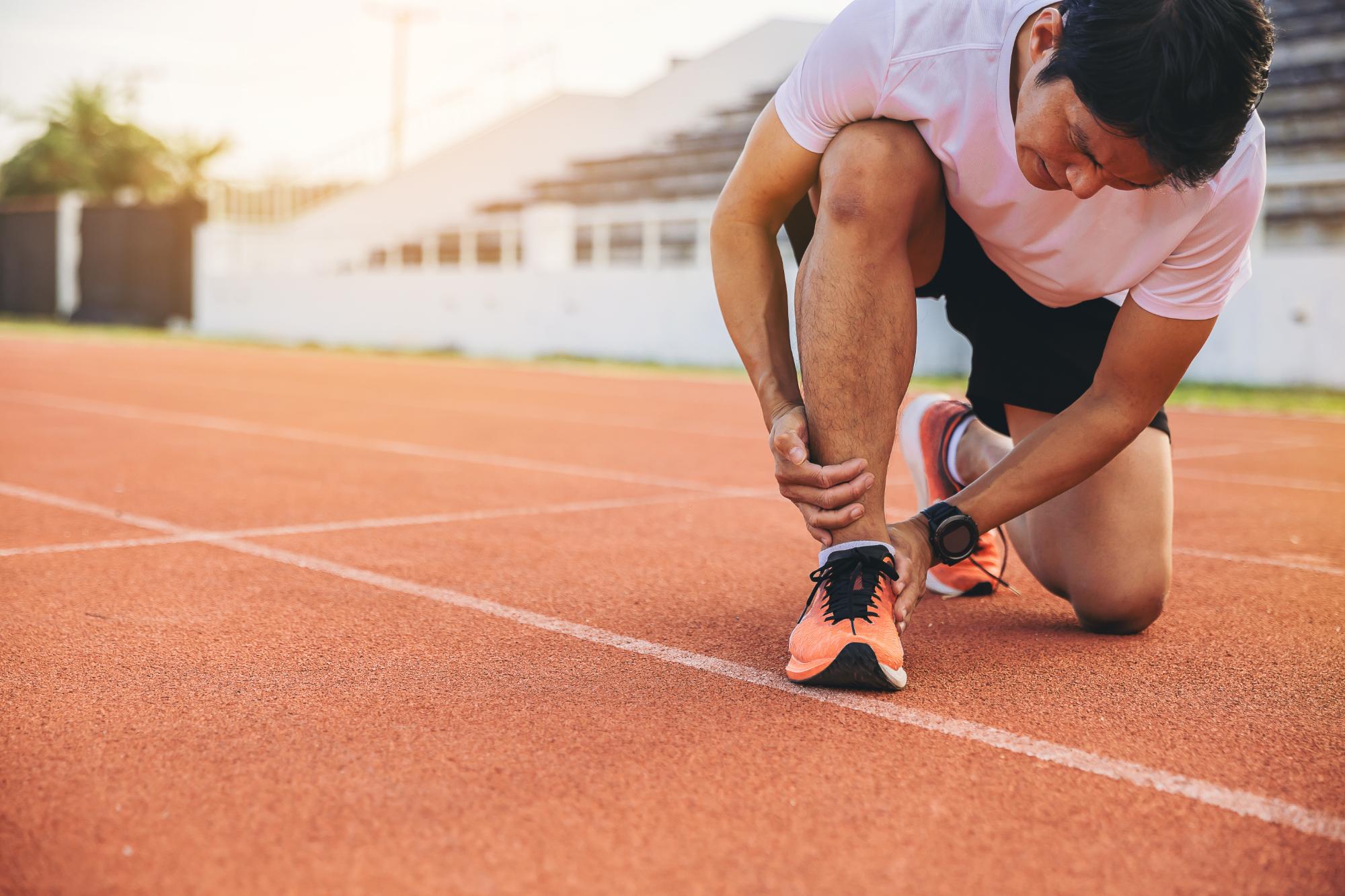 A runner on a track bends down to touch their sprained right ankle