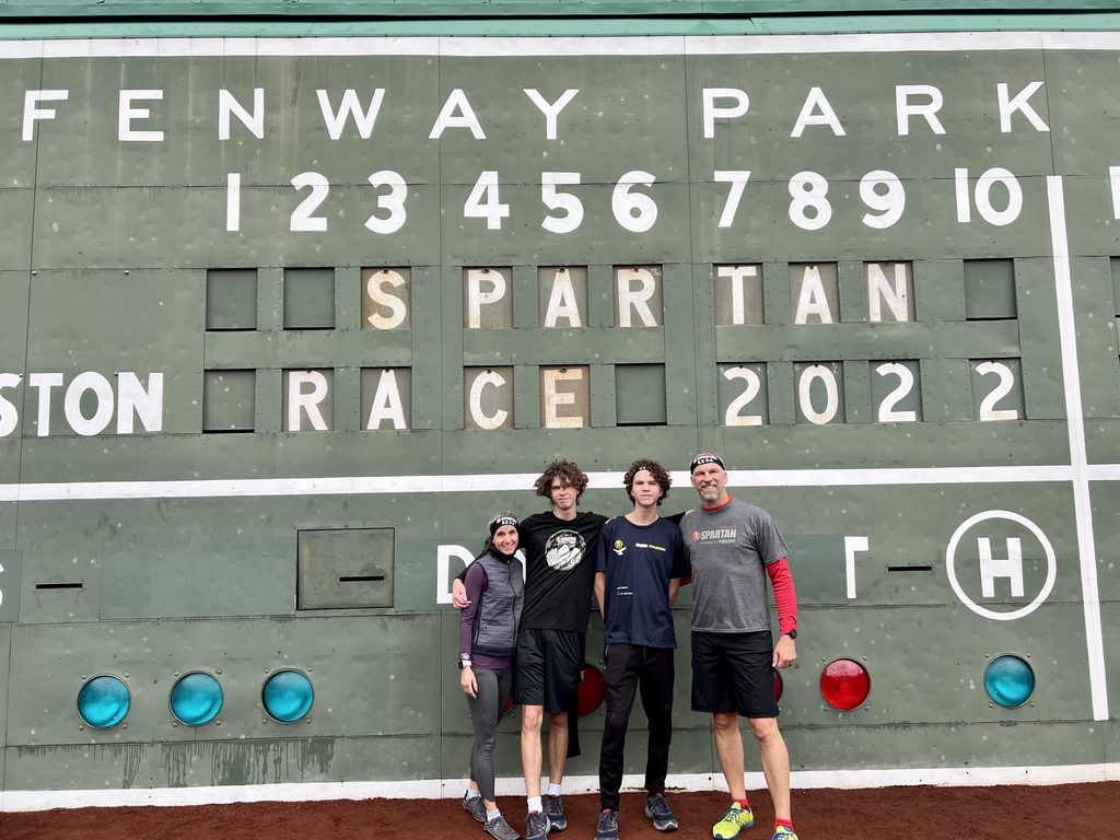 Andrea Wonderlin with her husband and two sons in front of the Fenway Park sign that says "Spartan Race 2022"